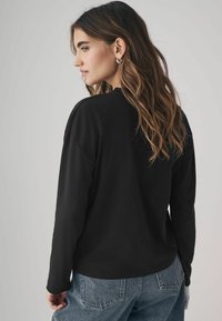 Maglietta nera a maniche lunghe con vestibilità comoda e scollo rotondo. Abbinata a pantaloni in denim azzurri, che mostrano un look informale.