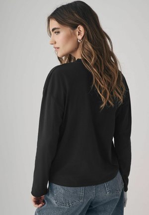 Schwarzes Langarmshirt mit lockerem Schnitt und rundem Ausschnitt. Kombiniert mit hellblauen Jeans, die einen lässigen Look zeigen.