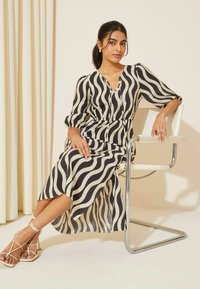 Rochie midi cu dungi alb-negru, cu o croială lejeră, decolteu în V și mâneci puff, asortată cu sandale bej cu bretele.