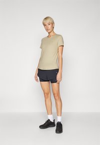 T-shirt kaki à manches courtes avec un col rond, associé à un short de sport noir et des chaussures noires, avec des chaussettes blanches à la cheville.