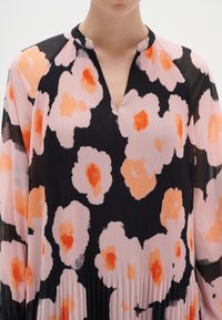 Blommönstrad klänning i rosa, orange och svart. Har en plisserad yta och en partiell V-ringning. Långa ärmar.