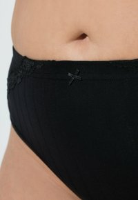 Zwarte onderbroek met een gestructureerd ribbenontwerp. De tailleband is accentueert met kant en een klein satijnen strikje.
