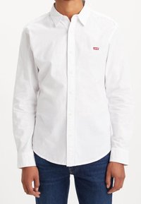 Camicia bianca a maniche lunghe con colletto, caratterizzata da un piccolo logo rosso Levi's sul petto sinistro e un orlo curvo.
