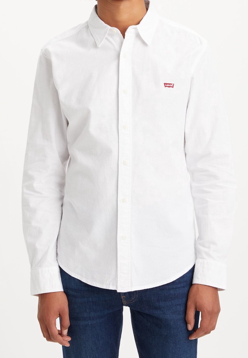 Camicia bianca a maniche lunghe con colletto, caratterizzata da un piccolo logo rosso Levi's sul petto sinistro e un orlo curvo.