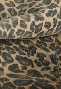 Tessuto con stampa leopardata su sfondo beige e macchie nere, caratterizzato da una trama testurizzata, con pieghe e dettagli di cucitura.