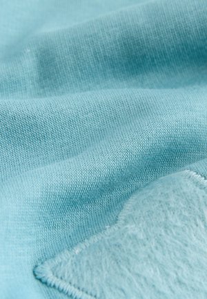 Tela azul claro con una textura suave y un patrón de punto visible, que presenta un parche suave y aterciopelado en un tono contrastante en un lado.