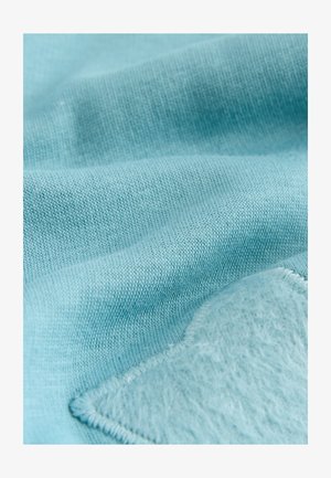 Hele sinine kangas, millel on sile tekstuur ja nähtav kootud muster, ühelt poolt on pehme, udune laik kontrastses toonis.