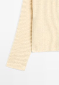 Beige geribbelde trui met lange mouwen, textuurstof en een rechte zoom. De stof vertoont fijne verticale lijnen.