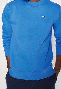 Sudadera azul con cuello redondo, puños y dobladillo acanalados, con un pequeño logo en el pecho. Tela suave, ajuste casual.