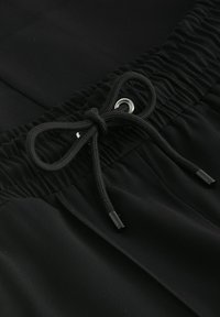 Svarta shorts med elastisk midja och dragsko trätt genom en silverfärgad ögla och svarta plastspetsar, tillverkade av ett mjukt tyg.