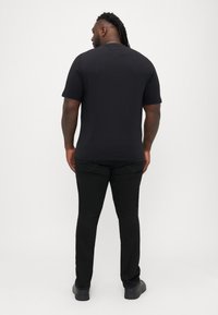 Μαύρη κοντομάνικη μπλούζα, εφαρμοστή σχεδίαση, λεία υφή. Φορεμένη με μαύρο παντελόνι, διακριτές ραφές και επίπεδα μαύρα παπούτσια.