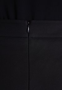 Černá oděvní látka se středovým zadním švem a malým černým zipem na horním konci švu.