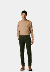 Beige Langarmshirt, kombiniert mit dunkelgrüner Hose und einem gemusterten Gürtel. Braune Stiefel runden das Outfit ab. Der Stoff hat eine glatte Textur.