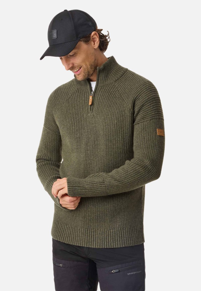 Olive green, ribbed-knit sweater with a quarter zipper and reinforced seams. Features a leather tag on the left sleeve. Worn with black cap.