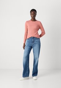 Pulover tricotat roz cu mâneci lungi, combinat cu blugi pal cu picior larg și adidași albi. Design simplu și stil casual.