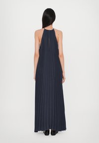 Abito maxi blu navy plissettato con collo halter e dettaglio a chiave sulla schiena. Tessitura liscia, tessuto fluido, taglio fino alla caviglia e senza chiusure visibili.