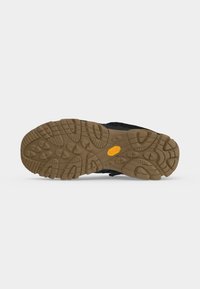 Semelle crantée d'une chaussure noire avec une semelle extérieure en caoutchouc marron présentant des rainures profondes et un logo Vibram jaune au centre.