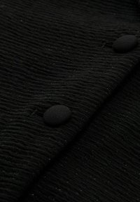 Tessuto nero con texture che presenta una superficie ondulata, arricchita da bottoni neri rotondi e sottili scintillii.