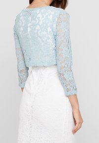 Lichtblauwe kanten cropped jack met lange mouwen, ingewikkelde bloemenpatronen, gecombineerd met een gestructureerde witte kanten rok.