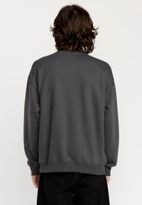 Gray sweatshirt with a crew neck, dropped shoulders, and ribbed cuffs. Made of soft fabric, it features a minimalistic design without patterns.