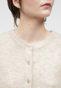 Helle beige Strickjacke mit rundem Ausschnitt, aus einem weichen, strukturierten Stoff und drei kleinen Knöpfen entlang der Vorderblende.