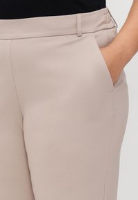 Beige stoffbukser med en jevn tekstur, med en elastisk midje og en sidelomme. Enkelt design uten mønstre eller aksenter.