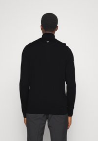 Sweater preto de mangas compridas com colarinho alto e design minimalista. Apresenta um pequeno logotipo branco nas costas e punhos e barra canelados.