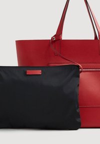 Bolso tote de cuero rojo con doble asa y bolsillo exterior, acompañado de un estuche negro con cremallera desmontable en la parte delantera.