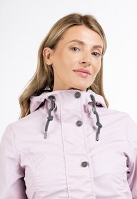 Giacca impermeabile rosa chiaro con cappuccio, dotata di cordini grigi, bottoni a scatto e dettagli arricciati sui lati.