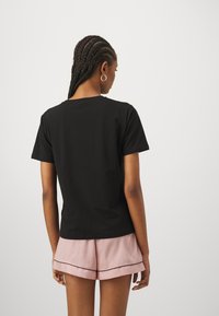 Black short-sleeve T-shirt made of cotton. Round neckline and relaxed fit. Worn with pink shorts featuring a black trim.