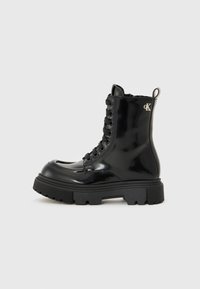 Bottines en cuir verni noir à lacets avec une semelle épaisse, dotées d'un accent logo et d'un soutien renforcé à la cheville.