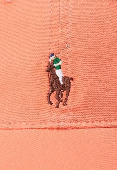 Kondom i korall med en brodert brun polo-spiller og hest logo. Har synlige sømmer og en strukturert design.