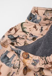 Tiermusterstoff in sanftem Beige mit verschiedenen illustrierten Tieren. Graue Fleece-Innenseite und goldene Druckknöpfe runden das Design ab.