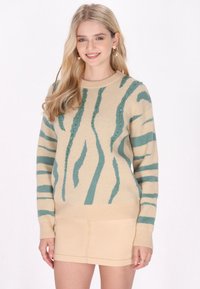 Maglione beige con strisce turchesi e paillettes. Presenta un colletto e polsini a costine. Abbinato a una gonna beige chiaro.
