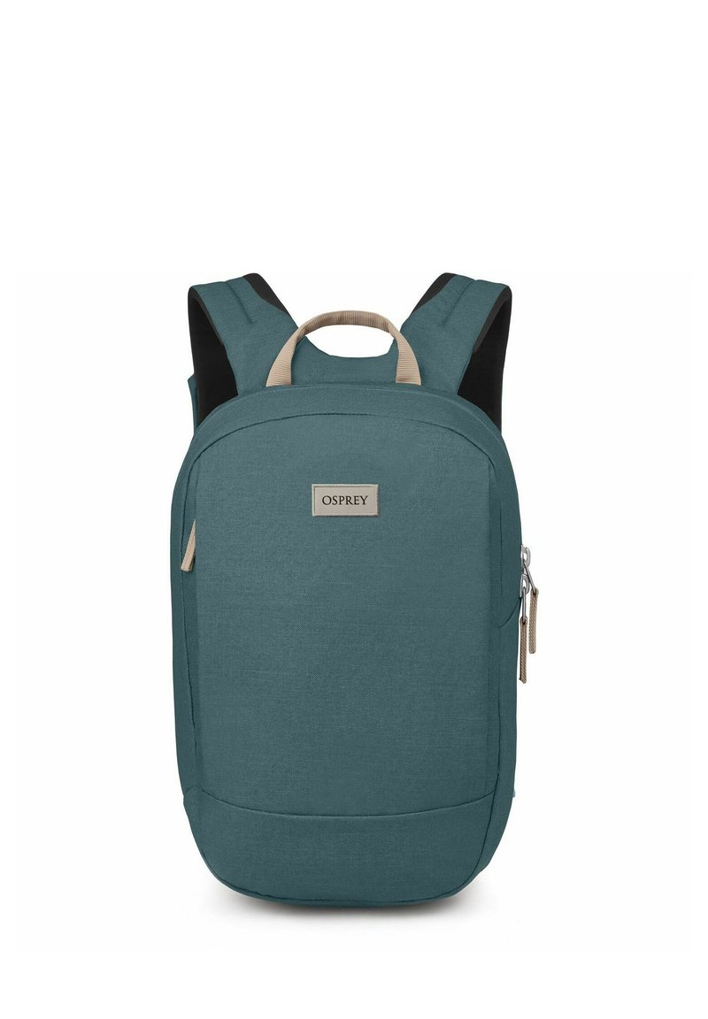 Mochila de tela en color teal con forma rectangular, detalles en color beige y correas para los hombros acolchadas. Cuenta con un bolsillo con cremallera y una etiqueta.