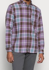 Koszula w kratkę z długim rękawem w kolorach purpurowym, brązowym i turkusowym, z zapinaniem na guziki z przodu, kołnierzykiem i jedną kieszenią na piersi.