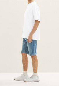 Camiseta blanca de manga corta combinada con pantalones cortos de mezclilla azules, zapatillas blancas y calcetines de longitud media, presentada sobre un fondo claro.