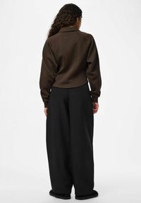 Veste courte marron avec col et manches longues, associée à un pantalon noir ample. Tissu doux, design minimaliste et détails de couture subtils.