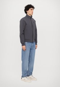 Grå jakke med høy krage, frontlås og elastiske mansjetter. Sammen med lyseblå løstsittende jeans og hvite sneakers.