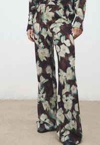 Pantalones de pierna ancha con un patrón floral en tonos de verde, crema y marrón. Fabricados en un tejido ligero con una textura suave.