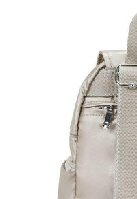 Srebrny tekstylny plecak z kieszenią na zamek i regulowanym paskiem. Charakteryzuje się gładkim, błyszczącym wykończeniem oraz małym ozdobnym elementem metalowym.