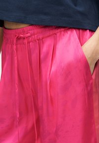 Ροζ παντελόνι από σατέν με ελαστική μέση και πλαϊνές τσέπες, με λεία υφή και διακριτικά μοτίβα σε διαφορετικές αποχρώσεις.