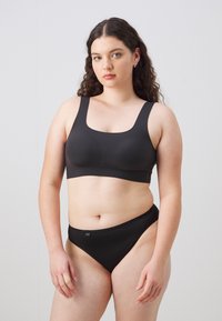 Zwarte sportbeha met brede bandjes en een gladde, elastische textuur, gecombineerd met bijpassende zwarte bikini-stijl onderkant met een klein logo-detail.