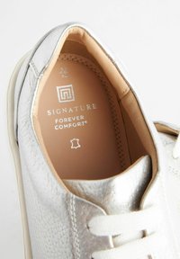 Silver sneaker featuring a textured finish, white laces, and a padded insole with branding details embossed in silver.