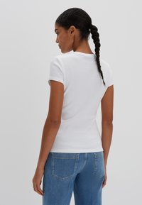 T-shirt bianco a maniche corte con una vestibilità aderente, abbinato a jeans di denim blu, che mostrano una texture liscia e un design minimalista.