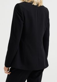 Svart skräddarsydd blazer med en slim fit, strukturerade axlar och en mjuk textur, med en enda slits bak och ingen synlig hårdvara.