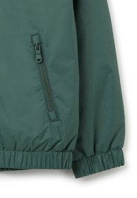 Grüne, leichte Jacke mit Reißverschlusstasche, elastischen Bündchen und Saum. Der Stoff hat eine glatte Textur und eine leicht glänzende Oberfläche.