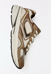 Baskets de sport marron et beige avec des panneaux en mesh et cuir, lacets blancs, et une semelle épaisse en caoutchouc blanc avec crampons noirs.
