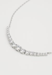 Collier en argent présentant un design courbé orné de pierres précieuses transparentes circulaires, augmentant en taille, avec une chaîne délicate.