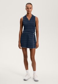 Mornarsko modra brezrokavna polo obleka z V-izrezom, teksturiranimi črtami in zavojem na krilu, ki vključuje gumb in kontrastno obrobo.